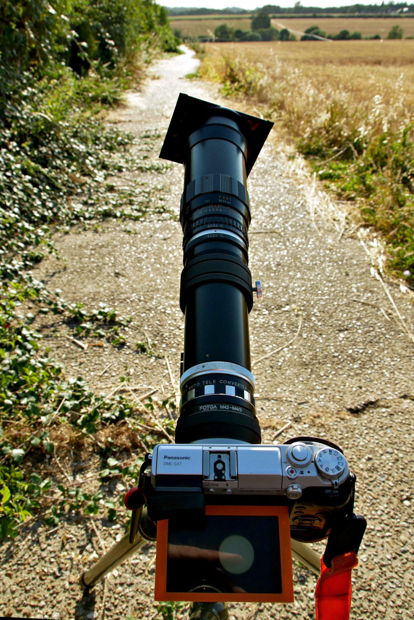 2026-08-12 Lumix DMC-GX7 camera with Hanimex 400mm lens and Tamron 2x Teleconverter mounted on Benbo Trekker tripod, with generic Arca-type quick release. Sun filter is a 90 mm x 110 mm welding glass, glued to a 72 mm - 82 mm step-up ring using black silicone bath sealer.